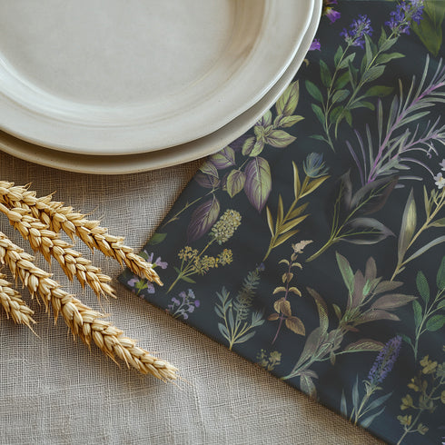 Set of four dark charcoal cloth napkins with a repeating pattern of muted purple, green, and gold herbs and flowers in an elegant botanical design.