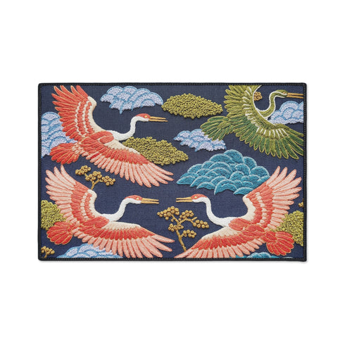 Grimoire and Goblet chinoiserie flying crane faux embroidery doormat featuring three cranes in coral blush and jade green soaring across deep navy background with teal scalloped clouds golden bonsai branches and olive foliage. Printed polyester entryway mat with non-slip rubber backing and black trim. Available 24x18 and 36x24 inches. Asian inspired Japanese crane design housewarming gift home decor