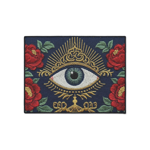 A rectangular navy blue Grimoire and Goblet doormat featuring a large central evil eye motif with a green iris and antique gold radiating lashes. The eye is surrounded by ornate gold filigree and four red peonies with green leaves in the corners. The design utilizes a high-quality 2D print technique to mimic the visual texture of vintage needlepoint embroidery, creating a trompe-l'œil effect on a flat 100% polyester surface.