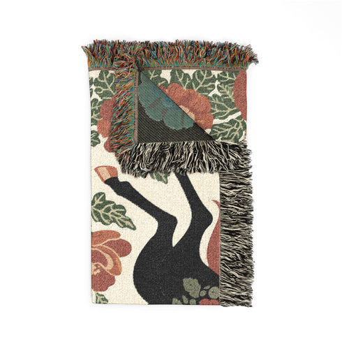 A woven cotton throw blanket by Grimoire and Goblet featuring two rearing horses facing each other in a symmetrical folk art design. One horse is charcoal black with rust floral detailing; the other is navy blue with teal floral detailing. They are framed by large rust-colored peonies and green leafy vines on a cream background. The blanket features a multicolor fringe edge. Perfect for dark academia and cottagecore aesthetics.