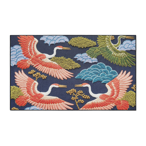 Grimoire and Goblet chinoiserie flying crane faux embroidery doormat featuring three cranes in coral blush and jade green soaring across deep navy background with teal scalloped clouds golden bonsai branches and olive foliage. Printed polyester entryway mat with non-slip rubber backing and black trim. Available 24x18 and 36x24 inches. Asian inspired Japanese crane design housewarming gift home decor