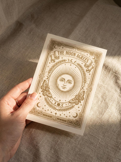 Grimoire and Goblet greeting card featuring a vintage woodcut style illustration of a radial sun with a serene human face. The sun is flanked by two Luna moths and sits above a Triple Moon symbol. A banner above reads THE MOON AGREES in gothic font. Printed in burnished gold tones on cream paper. Interior text reads Yours in this lifetime and the next. Dark Academia and Whimsigoth aesthetic stationery 5x7 card with matching envelope for gothic romance or altar decor.