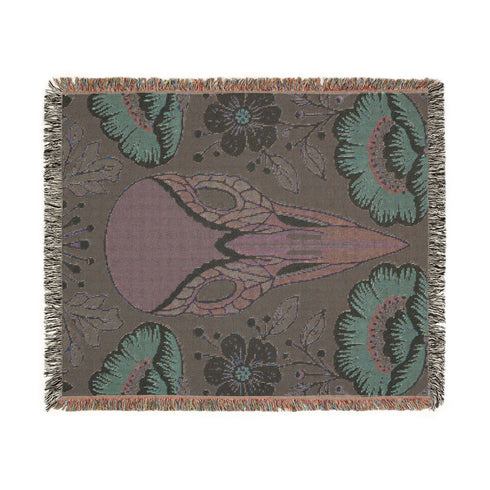 A midnight navy woven cotton blanket featuring a large central raven skull surrounded by rust and ochre flowers, and sage green ferns. Crescent moons are located in the four corners. The blanket has a colorful fringed edge and a textured, loomed appearance. Displayed as a premium gothic botanical home decor piece by Grimoire and Goblet.