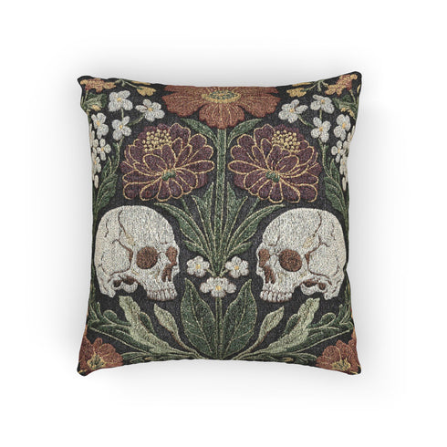 A Grimoire and Goblet woven tapestry pillow featuring a symmetrical dark botanical design. Two beige human skulls face each other in profile against a dark charcoal background. They are surrounded by deep burgundy dahlia flowers, sage green leaves, and small white floral clusters in an Arts and Crafts style. The texture is a visible fabric weave. The design is double-sided, square, and filled.