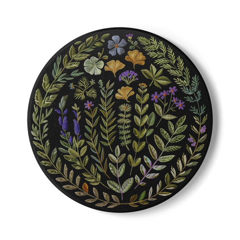 Circular ceramic coaster with black background featuring intricate botanical illustrations of various herbs, flowers and leaves in green, purple and gold colors with white ceramic edge and cork backing.