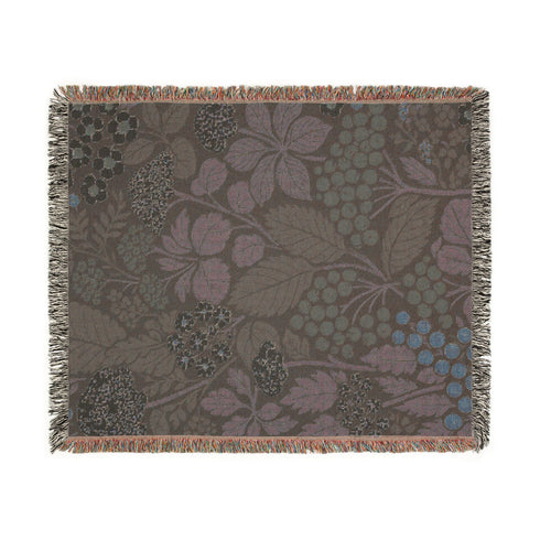 A Grimoire and Goblet luxury woven throw blanket featuring a dark botanical design. The Jacquard cotton tapestry showcases cream elderflower clusters and rust-colored berries against a deep black background. Sage green leaves interweave throughout the floral pattern. The blanket is finished with multicolored fringe edges. A moody cottagecore aesthetic piece ideal for dark academia decor.
