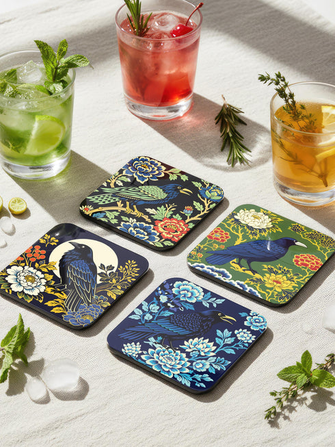 Grimoire and Goblet set of 4 glossy square coasters featuring Chinoiserie style raven illustrations. 1: Navy blue with blue floral pattern and raven. 2: Navy background with black raven, white full moon, and red berries. 3: Moss green background with blue bird and yellow chrysanthemums. 4: Black background with teal-winged raven and red peonies. MDF hardboard with cork backing. Flat vector botanical art style.