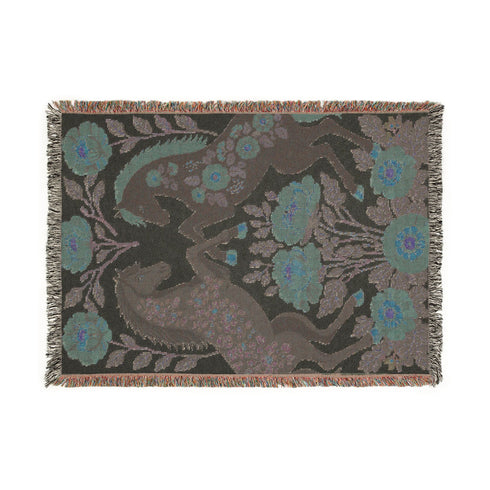 A woven cotton throw blanket by Grimoire and Goblet featuring two rearing horses facing each other in a symmetrical folk art design. One horse is charcoal black with rust floral detailing; the other is navy blue with teal floral detailing. They are framed by large rust-colored peonies and green leafy vines on a cream background. The blanket features a multicolor fringe edge. Perfect for dark academia and cottagecore aesthetics.