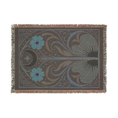 A luxurious, intricately woven jacquard blanket from Grimoire and Goblet. The design is a symmetrical Art Nouveau botanical pattern on a dark teal background. A central stem with green leaves swirls upwards, flanked by two large, rust-orange flowers. At the top, a golden crescent moon and star sparkle. A fan-like, sun-inspired motif rests at the base. The entire piece, crafted from 100% cotton, is framed by a decorative gold border and a multi-colored fringe.