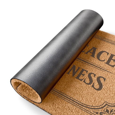 A high-angle close-up view of a Grimoire and Goblet luxury coir doormat. The mat features the phrase Enter in Peace Leave in Kindness painted in bold, Gothic-style black typography against the natural golden-brown texture of coconut husks. The text is enclosed in an intricate Victorian ornamental border with filigree corner flourishes. The texture appears coarse, durable, and dense, typical of high-quality tufted coconut fiber entry mats. The design evokes a Dark Academia and witchy aesthetic.
