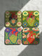 A set of four premium 4x4 inch anatomical heart coasters from Grimoire and Goblet. Each square coaster is made of masonite hardboard with a high-gloss finish and a non-slip cork base. The designs feature intricate biological heart illustrations with folk-art floral motifs in vibrant crimson, pink, yellow, and purple against mossy green and deep teal backgrounds. The high-fidelity print mimics a luxury embroidered texture, perfect for a cardiology gift or dark academia home decor.