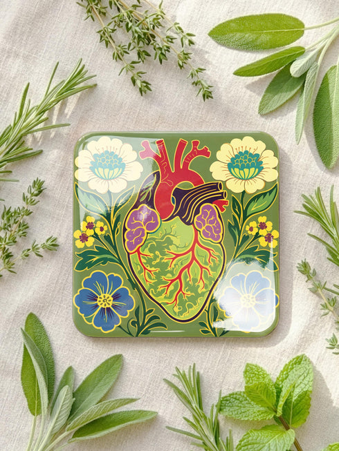 A set of four premium 4x4 inch anatomical heart coasters from Grimoire and Goblet. Each square coaster is made of masonite hardboard with a high-gloss finish and a non-slip cork base. The designs feature intricate biological heart illustrations with folk-art floral motifs in vibrant crimson, pink, yellow, and purple against mossy green and deep teal backgrounds. The high-fidelity print mimics a luxury embroidered texture, perfect for a cardiology gift or dark academia home decor.
