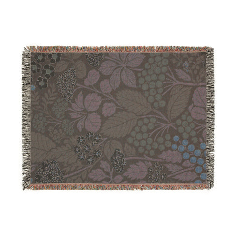 A Grimoire and Goblet luxury woven throw blanket featuring a dark botanical design. The Jacquard cotton tapestry showcases cream elderflower clusters and rust-colored berries against a deep black background. Sage green leaves interweave throughout the floral pattern. The blanket is finished with multicolored fringe edges. A moody cottagecore aesthetic piece ideal for dark academia decor.