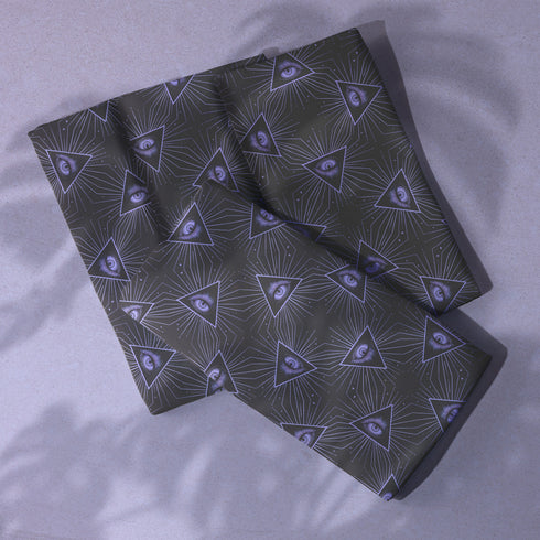 Set of four charcoal-colored cloth napkins with a repeating pattern of triangular all-seeing eyes in purple, surrounded by radiating lines and small star-like accents.