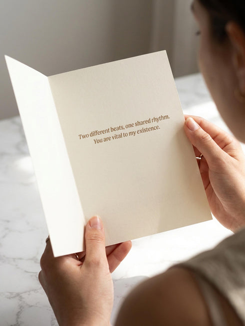 A vintage-style greeting card titled "DE HUMANI CORDIS" featuring a medical illustration of two anatomical hearts connected by a single looped blood vessel. The hearts are drawn in a sepia and crimson woodcut style on a cream background mimicking aged parchment. Text below reads "Fig. 14: The Twin Pulse." The card evokes a dark academia or cottagecore aesthetic. Inside text reads "Two different beats, one shared rhythm.