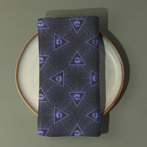 Set of four charcoal-colored cloth napkins with a repeating pattern of triangular all-seeing eyes in purple, surrounded by radiating lines and small star-like accents.