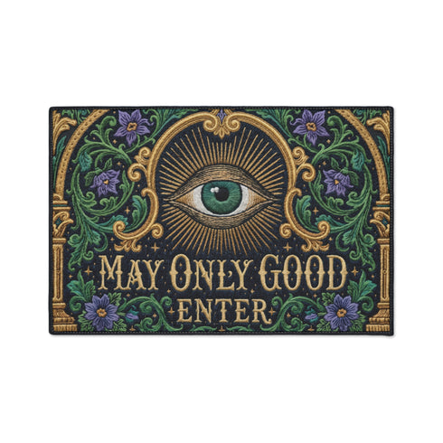 Rectangular doormat printed on a deep black ground with a faux embroidery effect that imitates antique crewelwork. A large green eye sits at the center within an antique gold radial sunburst, with ornate gold serif lettering below reading MAY ONLY GOOD ENTER. Green acanthus leaf scrollwork and antique gold architectural columns run along the borders, accented with small five petaled purple flowers. A sleek black trim frames all four edges of the flat printed surface.