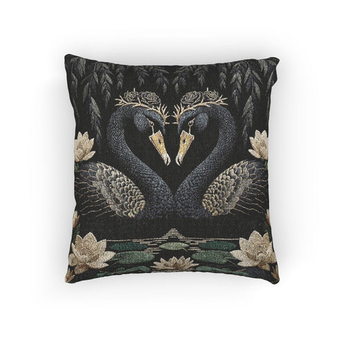 A double-sided woven jacquard throw pillow by Grimoire and Goblet measuring 17 by 18 inches. The tactile tapestry design features two black swans facing each other, their gracefully curved necks forming a subtle heart shape. Each swan wears a delicate floral crown in gold and cream tones. They float on a dark pond adorned with muted green lily pads and cream water lilies. The textured surface is woven from cotton and polyester threads.