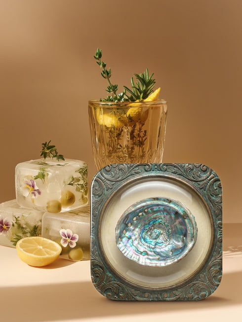 A high-fidelity 2D Trompe-l’œil print on a set of four 4x4 inch square coasters. Each coaster features a centralized sea specimen—a scallop, an oyster with a pearl, a pink conch, and an abalone—centered within an ornate, circular Victorian scrollwork frame. The design uses a faux-texture effect to mimic raised bronze and verdigris metal. The colors include aged gold, teal, and cream, creating a vintage museum specimen aesthetic