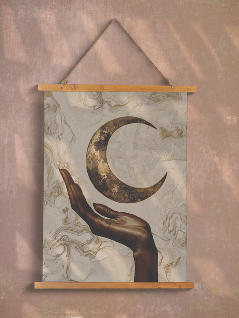 A wall tapestry featuring a bronze-colored hand reaching upward toward an antiqued gold crescent moon, set against a swirling ivory and gold marbled background, mounted between wooden dowels with twine.