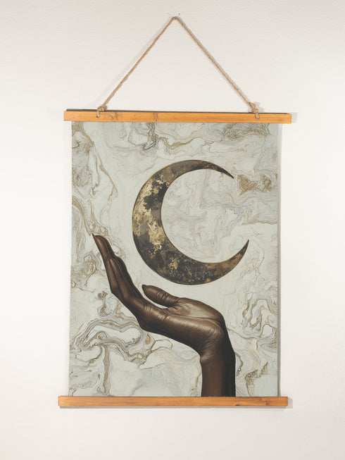 A wall tapestry featuring a bronze-colored hand reaching upward toward an antiqued gold crescent moon, set against a swirling ivory and gold marbled background, mounted between wooden dowels with twine.