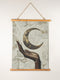 A wall tapestry featuring a bronze-colored hand reaching upward toward an antiqued gold crescent moon, set against a swirling ivory and gold marbled background, mounted between wooden dowels with twine.