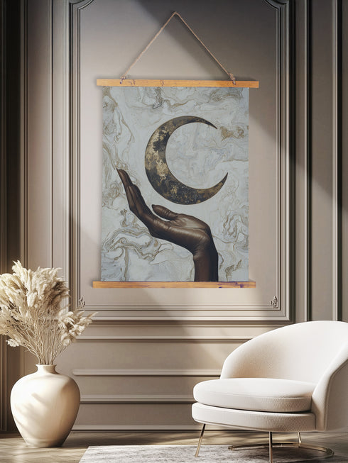 A wall tapestry featuring a bronze-colored hand reaching upward toward an antiqued gold crescent moon, set against a swirling ivory and gold marbled background, mounted between wooden dowels with twine.