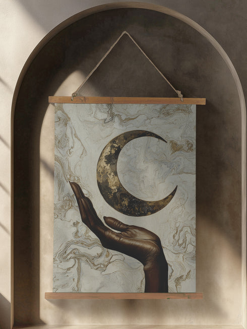 A wall tapestry featuring a bronze-colored hand reaching upward toward an antiqued gold crescent moon, set against a swirling ivory and gold marbled background, mounted between wooden dowels with twine.