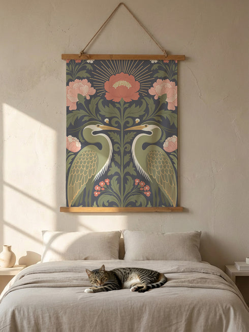 Vertical 26x36 inch wall tapestry by Grimoire and Goblet featuring a symmetrical design of two sage green herons facing each other. The birds are framed by dark green foliage, rust-colored berries, and large dusty pink peony flowers against a dark slate gray background. A golden radial sunburst sits at the top center. The smooth polyester fabric is suspended between two artisanal wooden dowels, hanging from a natural twine cord. The image features no background scene.Vertical 26x36 inch wall tapestry by Gri