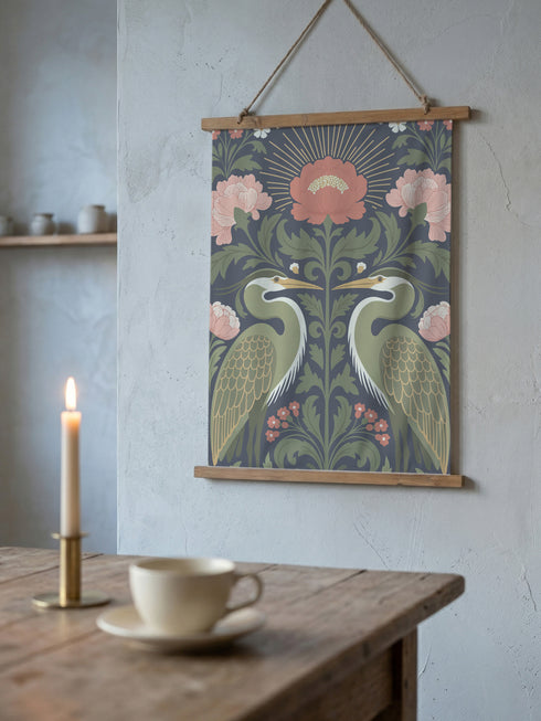 Vertical 26x36 inch wall tapestry by Grimoire and Goblet featuring a symmetrical design of two sage green herons facing each other. The birds are framed by dark green foliage, rust-colored berries, and large dusty pink peony flowers against a dark slate gray background. A golden radial sunburst sits at the top center. The smooth polyester fabric is suspended between two artisanal wooden dowels, hanging from a natural twine cord. The image features no background scene.