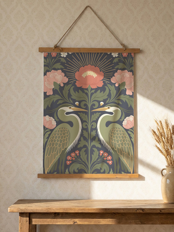 Vertical 26x36 inch wall tapestry by Grimoire and Goblet featuring a symmetrical design of two sage green herons facing each other. The birds are framed by dark green foliage, rust-colored berries, and large dusty pink peony flowers against a dark slate gray background. A golden radial sunburst sits at the top center. The smooth polyester fabric is suspended between two artisanal wooden dowels, hanging from a natural twine cord. The image features no background scene.