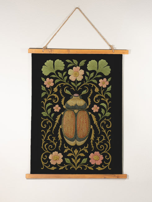 26x36 inch vertical wall tapestry printed on silky polyester fabric, featuring a detailed embroidered-style beetle surrounded by pink and green florals and curling botanical vines on a black background, with wooden hanger and twine at top and bottom. Art nouveau, vintage-inspired, cottagecore, gothic decor.