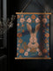 Large wall tapestry featuring a detailed rabbit portrait surrounded by copper and pink flowers on a deep teal background, mounted on wooden dowels with twine for hanging.