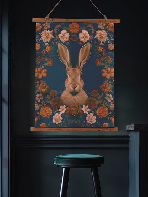 Large wall tapestry featuring a detailed rabbit portrait surrounded by copper and pink flowers on a deep teal background, mounted on wooden dowels with twine for hanging.