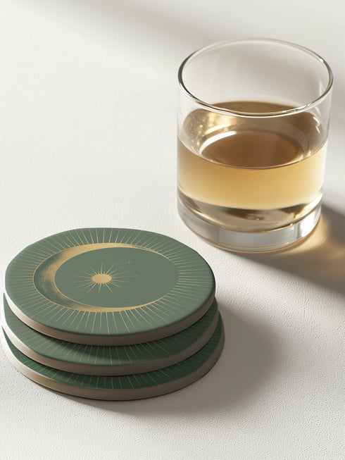 Round ceramic coaster with forest green background. Golden crescent moon embraces a sun at the center. Fine golden lines radiate outward, creating a sunburst pattern to the edge. White rim indicates cork backing. Coaster diameter is 4.04 inches.