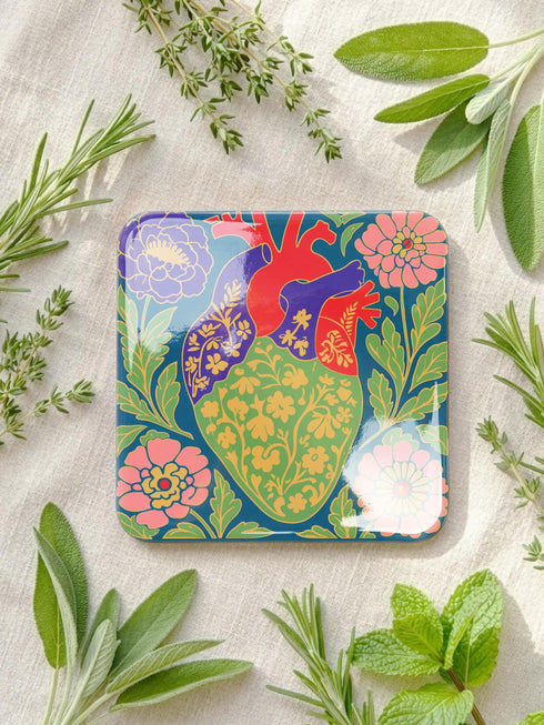 A set of four premium 4x4 inch anatomical heart coasters from Grimoire and Goblet. Each square coaster is made of masonite hardboard with a high-gloss finish and a non-slip cork base. The designs feature intricate biological heart illustrations with folk-art floral motifs in vibrant crimson, pink, yellow, and purple against mossy green and deep teal backgrounds. The high-fidelity print mimics a luxury embroidered texture, perfect for a cardiology gift or dark academia home decor.