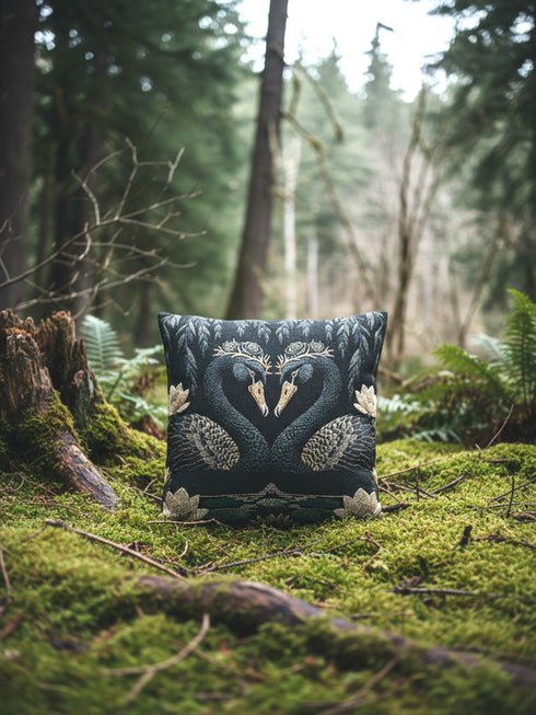 A double-sided woven jacquard throw pillow by Grimoire and Goblet measuring 17 by 18 inches. The tactile tapestry design features two black swans facing each other, their gracefully curved necks forming a subtle heart shape. Each swan wears a delicate floral crown in gold and cream tones. They float on a dark pond adorned with muted green lily pads and cream water lilies. The textured surface is woven from cotton and polyester threads.