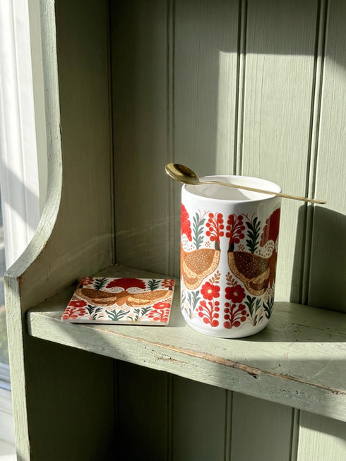 A detailed close-up of a luxury ceramic mug and matching square coaster set from Grimoire and Goblet. The items feature a vintage-style scientific illustration of a large moth with intricate wing patterns in earth tones of rust red and moss green, resting on stylized botanical foliage. The aesthetic is Dark Academia and Victorian Gothic. The mug is a large 15oz white ceramic vessel with a sturdy C-handle. The coaster is a glazed ceramic tile with a glossy finish.