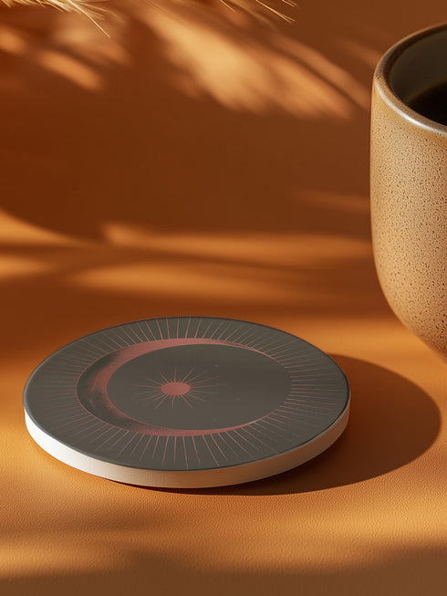 A round ceramic plate with a sleek design featuring a crescent moon and radiating lines in a muted red and black color scheme. The plate is set against a warm brown background with soft lighting, highlighting the celestial and minimalist aesthetic of the piece.
