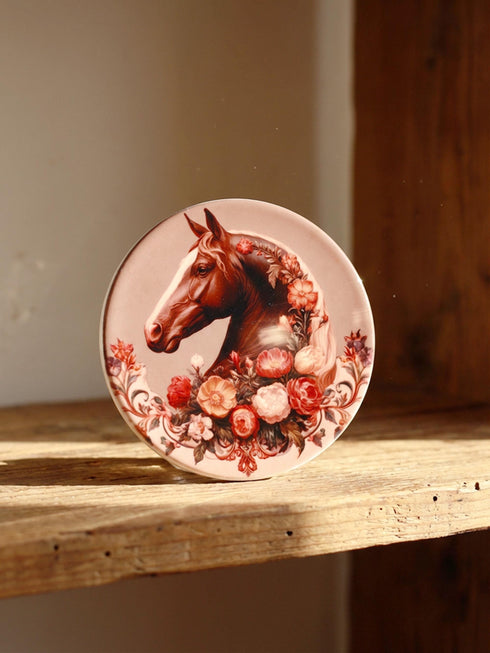 A round glazed ceramic coaster by Grimoire and Goblet featuring a vintage Victorian horse portrait design. The coaster has a high gloss porcelain-like finish and a natural cork bottom for furniture protection. The artwork depicts a dark bay horse head in profile surrounded by moody botanical flowers in shades of rust and deep red, evoking a dark academia and gothic cottagecore aesthetic. This 4x4 inch tile serves as a protective drink mat or decorative equine art accent.