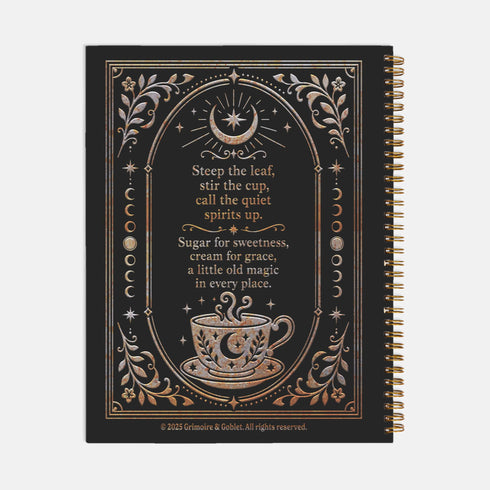 Spiral-bound recipe journal with a black cover and a metallic gold and silver design. The front reads Tea Leaves and Table Spells, Recipes for Sips, Sweets and Small Magic, framed by an arch, a crescent moon and star, moon phases, botanical sprigs, and a steaming teacup. The wire-O binding runs along one edge. Inside are blank fill-in recipe pages with lines for the recipe name, kitchen of origin, prep and cook time, servings, ingredients, and instructions.