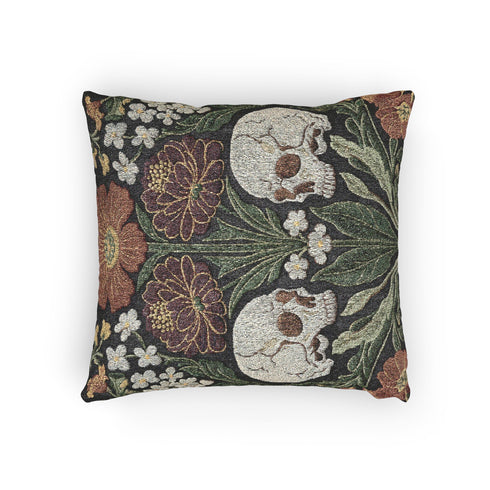A Grimoire and Goblet woven tapestry pillow featuring a symmetrical dark botanical design. Two beige human skulls face each other in profile against a dark charcoal background. They are surrounded by deep burgundy dahlia flowers, sage green leaves, and small white floral clusters in an Arts and Crafts style. The texture is a visible fabric weave. The design is double-sided, square, and filled.