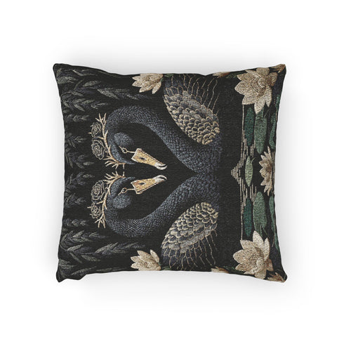 A double-sided woven jacquard throw pillow by Grimoire and Goblet measuring 17 by 18 inches. The tactile tapestry design features two black swans facing each other, their gracefully curved necks forming a subtle heart shape. Each swan wears a delicate floral crown in gold and cream tones. They float on a dark pond adorned with muted green lily pads and cream water lilies. The textured surface is woven from cotton and polyester threads.
