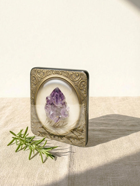 Grimoire and Goblet set of four square glossy coasters featuring high-resolution printed illustrations of raw crystals: purple amethyst, pink rose quartz, iridescent labradorite, and banded agate. Each gemstone is depicted inside a printed faux antique brass baroque frame with intricate scrollwork, set against a cream parchment background. The design is a flat 2D trompe l'œil print on hardboard, creating a realistic 3D specimen box illusion.
