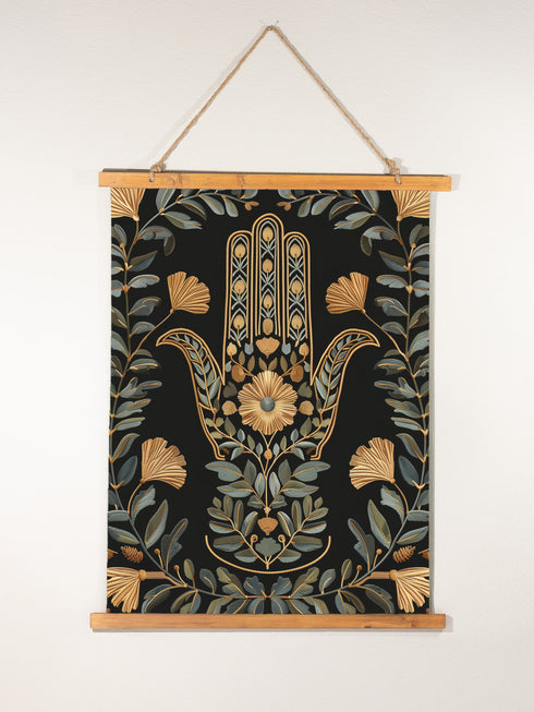 Botanical Hamsa wall tapestry featuring gold and teal design on black background, showing a protective hand symbol adorned with leaf motifs and floral elements, hanging from wooden dowels with natural twine.