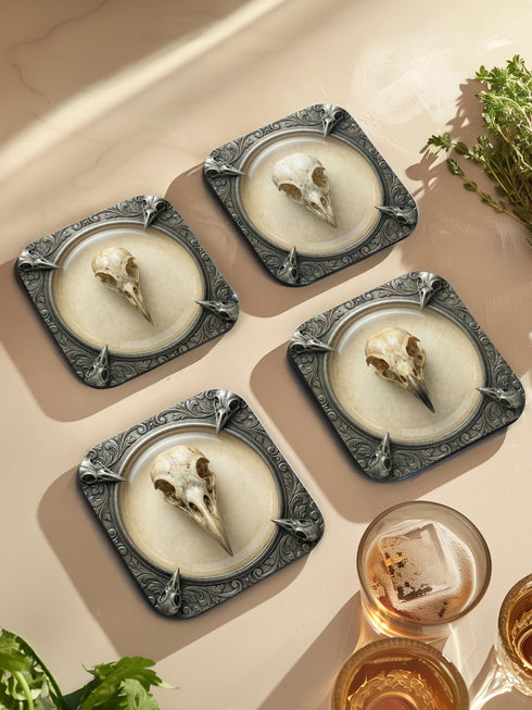 A set of four square 4x4 inch coasters by Grimoire and Goblet. Each features a unique avian skull specimen: a hooked raptor, a slender insectivore, a straight-billed corvid, and a scavenger. Designs are framed by silver faux-texture scrollwork on aged parchment. The coasters have a reflective high-gloss finish and tan cork backing. A perfect companion for a gothic goblet or grimoire study.