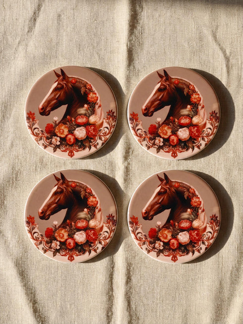 A round glazed ceramic coaster by Grimoire and Goblet featuring a vintage Victorian horse portrait design. The coaster has a high gloss porcelain-like finish and a natural cork bottom for furniture protection. The artwork depicts a dark bay horse head in profile surrounded by moody botanical flowers in shades of rust and deep red, evoking a dark academia and gothic cottagecore aesthetic. This 4x4 inch tile serves as a protective drink mat or decorative equine art accent.