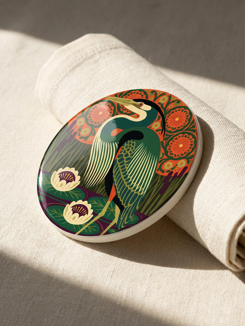 This set of four round ceramic coasters features a glossy, smooth, high-fidelity flat-printed surface. Each piece displays highly detailed Art Nouveau style illustrations of herons and egrets surrounded by stylized water lilies, chrysanthemums, and rich foliage. The vibrant, intricate color palette includes deep emerald greens, rich crimson reds, navy blues, and golden yellows. The sides are smooth, unprinted white ceramic, and the underside is fitted with a natural brown cork backing.