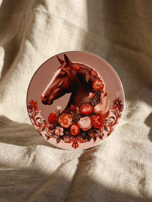 A round glazed ceramic coaster by Grimoire and Goblet featuring a vintage Victorian horse portrait design. The coaster has a high gloss porcelain-like finish and a natural cork bottom for furniture protection. The artwork depicts a dark bay horse head in profile surrounded by moody botanical flowers in shades of rust and deep red, evoking a dark academia and gothic cottagecore aesthetic. This 4x4 inch tile serves as a protective drink mat or decorative equine art accent.