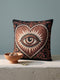 Square jacquard woven throw pillow measuring 17 by 18 inches. The design features a large central heart in rust and terracotta framing a detailed, unblinking eye with a black pupil, surrounded by cream colored jagged radiating rays. The solid black background is accented in the corners by ornate, curling cream botanical scrolls. Interlocking threads create a highly textured tapestry cloth, woven identically on the front and back faces, finished with a cleanly sewn closed edge.